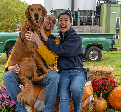 A golden retriever and its paw-rents sitting on a hay bale at Punkin Ale Fest at Dogfish Head iMilton Brewery in 2023