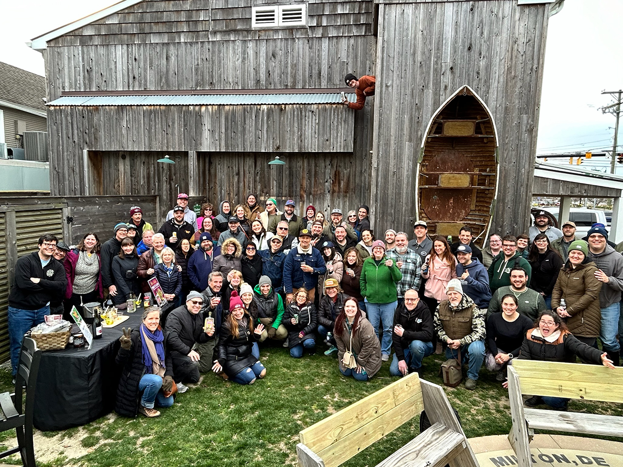 a large group of people standing in the Dogfish Head Inn courtyard against a weathered wood facade with row boat on the wall.