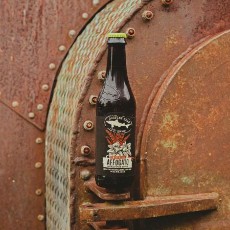 A bottle of Affogato World Wide Stout with industrial structures in the background