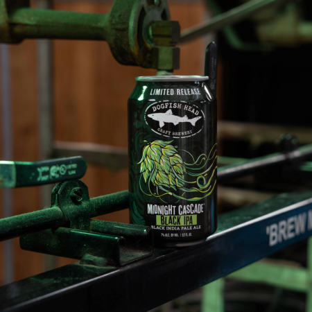 A can of Dogfish Head Midnight Cascade on top of a green bar in a brewery