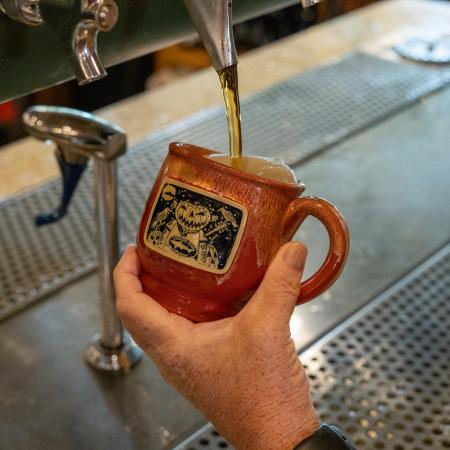 Orange ceramic Punkin Ale mug under a tap with beer pouring into it in a bar