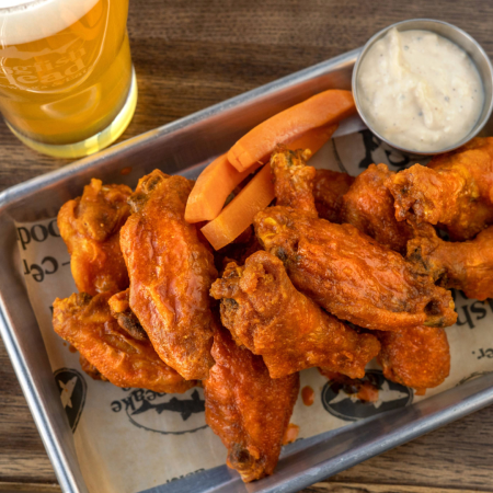 A dozen buffalo wings on a plate with a pint of beer next to it at Dogfish Head Brewings & Eats