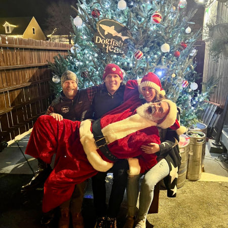 Dogfish Head coworkers with a man in a red suit sitting in front of a decorated holiday tree at Brewings & Eats in Rehoboth Beach, Delaware