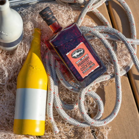 Bottle of Pawberry Ready-To-Pour cocktail on a deck with a boat behind it