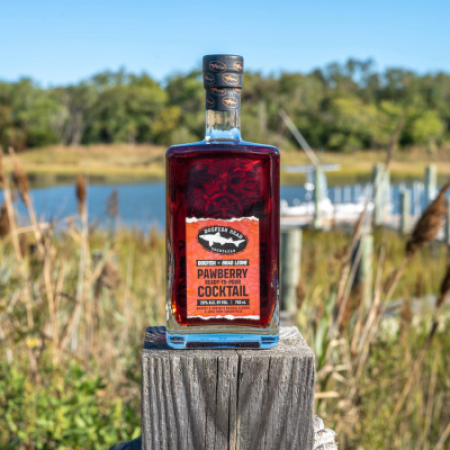 Bottle of Pawberry Ready-To-Pour cocktail on a deck with a marsh and a body of water behind it