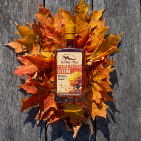 A bottle of Dogfish Head Maple Spiced Rum laying on a wooden deck with a bed of orange and yellow leaves under it