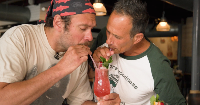 Dogfish Head's Sam Calagione and Brad Leone sipping on a pink cocktail, Pawberry Cocktail, in a hurricane glass at Chesapeake & Maine