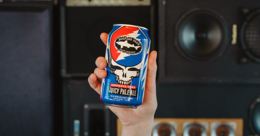 Dogfish Head x Grateful Dead Juicy Pale Ale 12 oz can in a hand with speakers behind it 