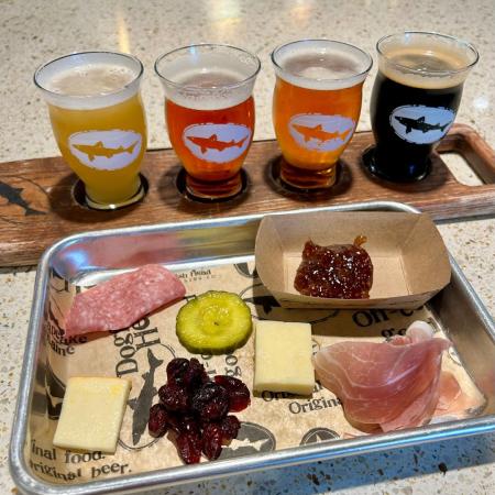 flight of 4 Dogfish Head beers in small tasting glasses next to a charcuterie board