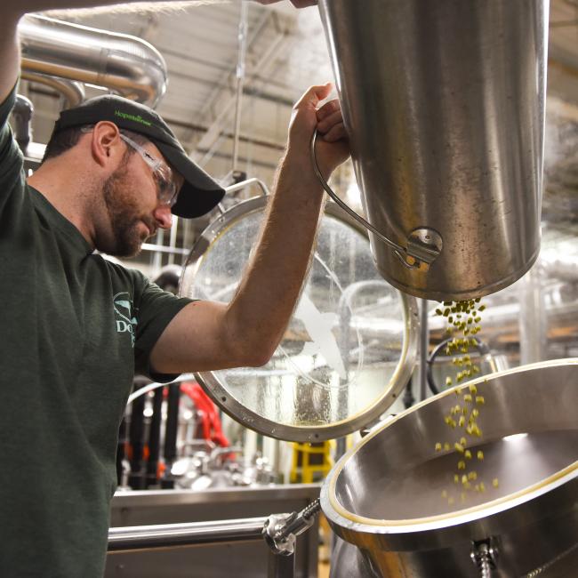 Innovation brewer Dan pouring hops into vessel